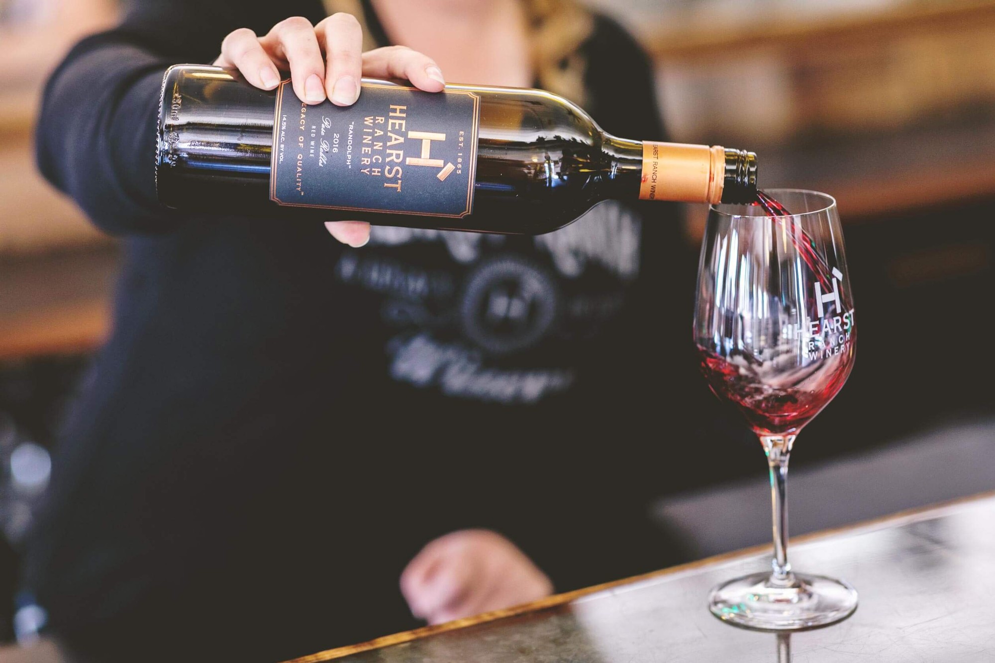 Woman pouring glass of Hearst Ranch Winery red wine.
